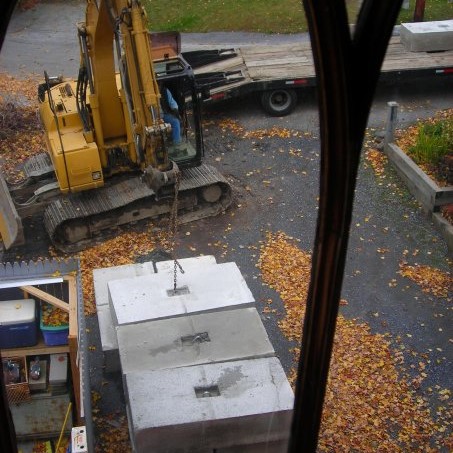Stack of concrete blocks near excavator and trailer with one more block.