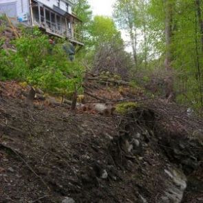 Broken concrete wall in landscape, house in near distance.