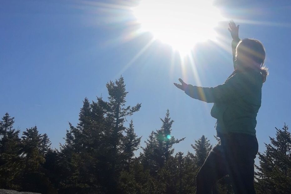 The author on a mountaintop wrapping her hands around the sun in the sky.